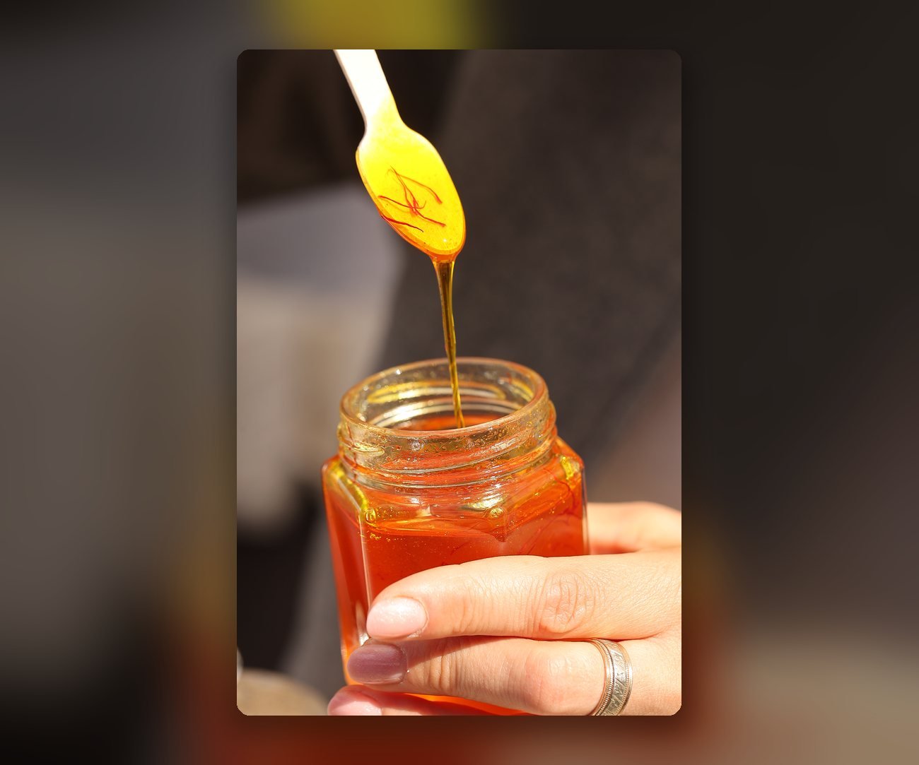 Linguriță cu miere și fire de șofran deasupra unui borcan